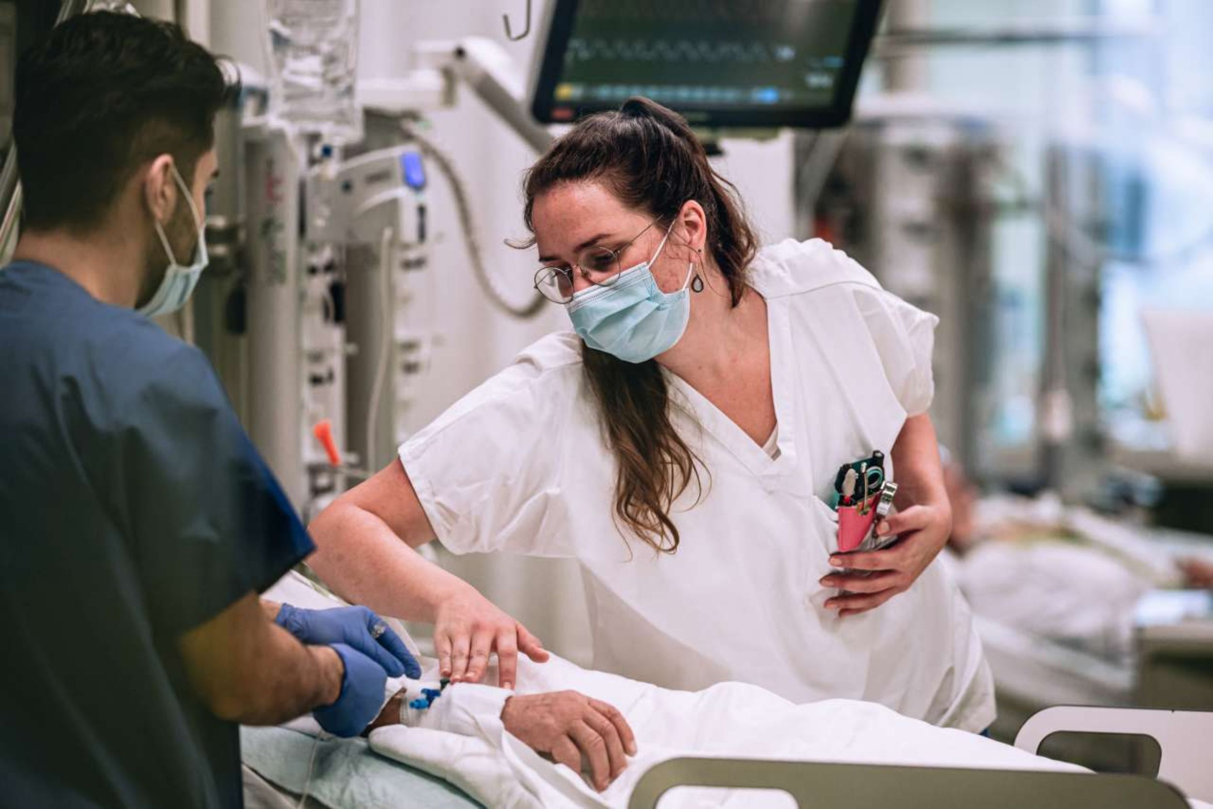 Pflegefachpersonen mit Mundschutz legen einem Patienten auf der Intensivstation eine Infusion.