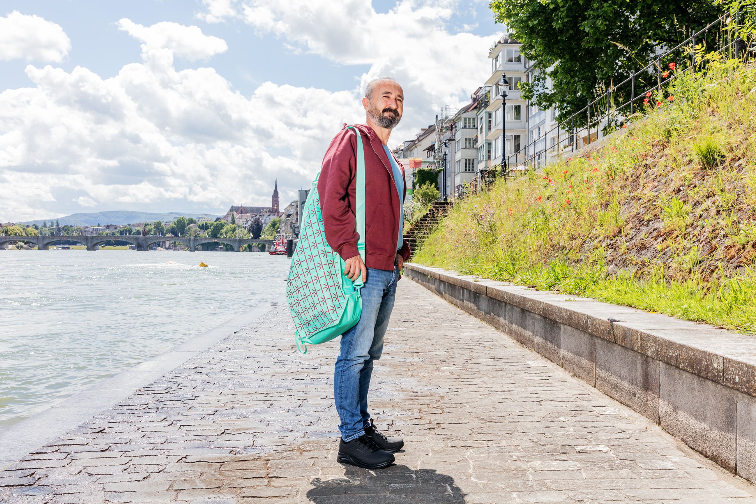 Mitarbeiter mit weinrotem USB-Merchandise Hoodie und türkisfarbenem Schwimmsack am Rheinufer
