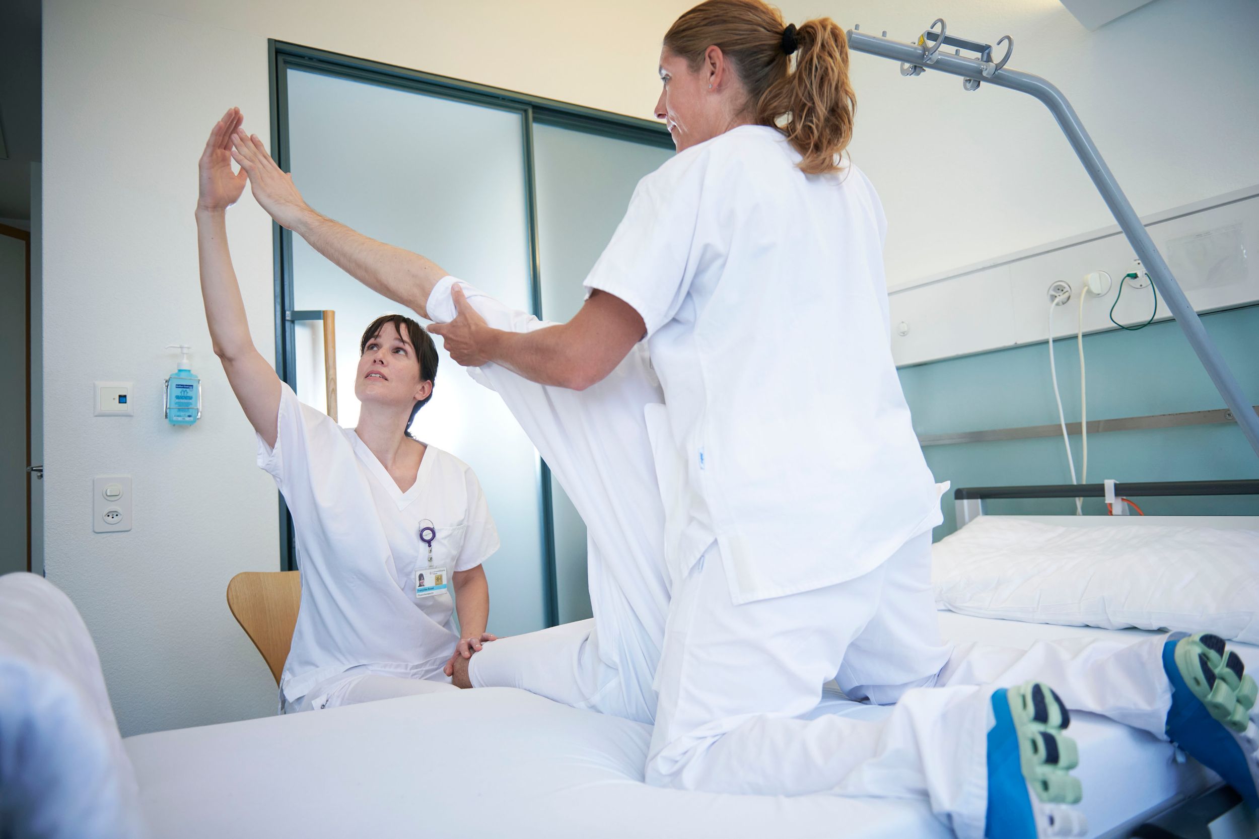 Physiotherapeutinnen behandeln Patient im Bett sitzend