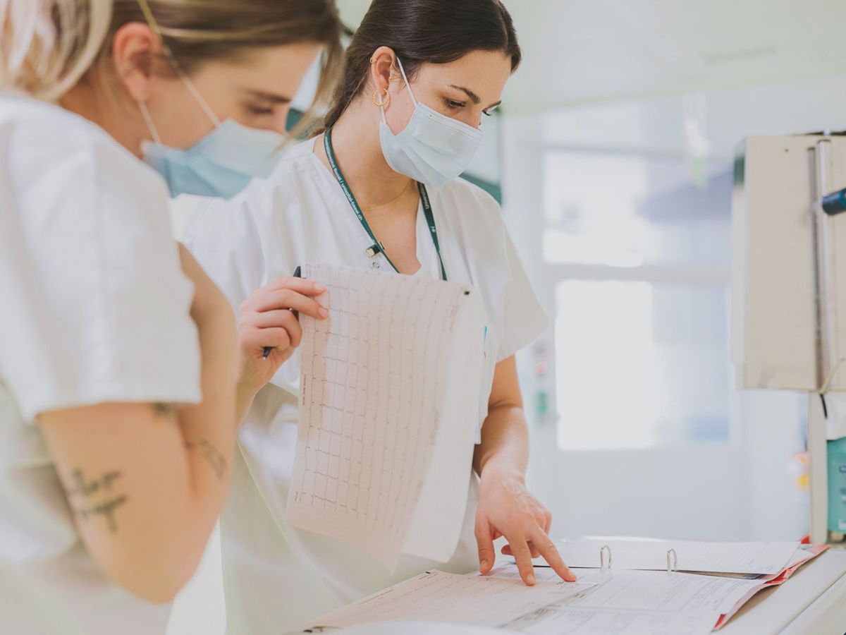Zwei Pflegefachkräfte mit Mundschutz schauen gemeinsam auf Patientendokumente und besprechen Einträge in einer Akte.