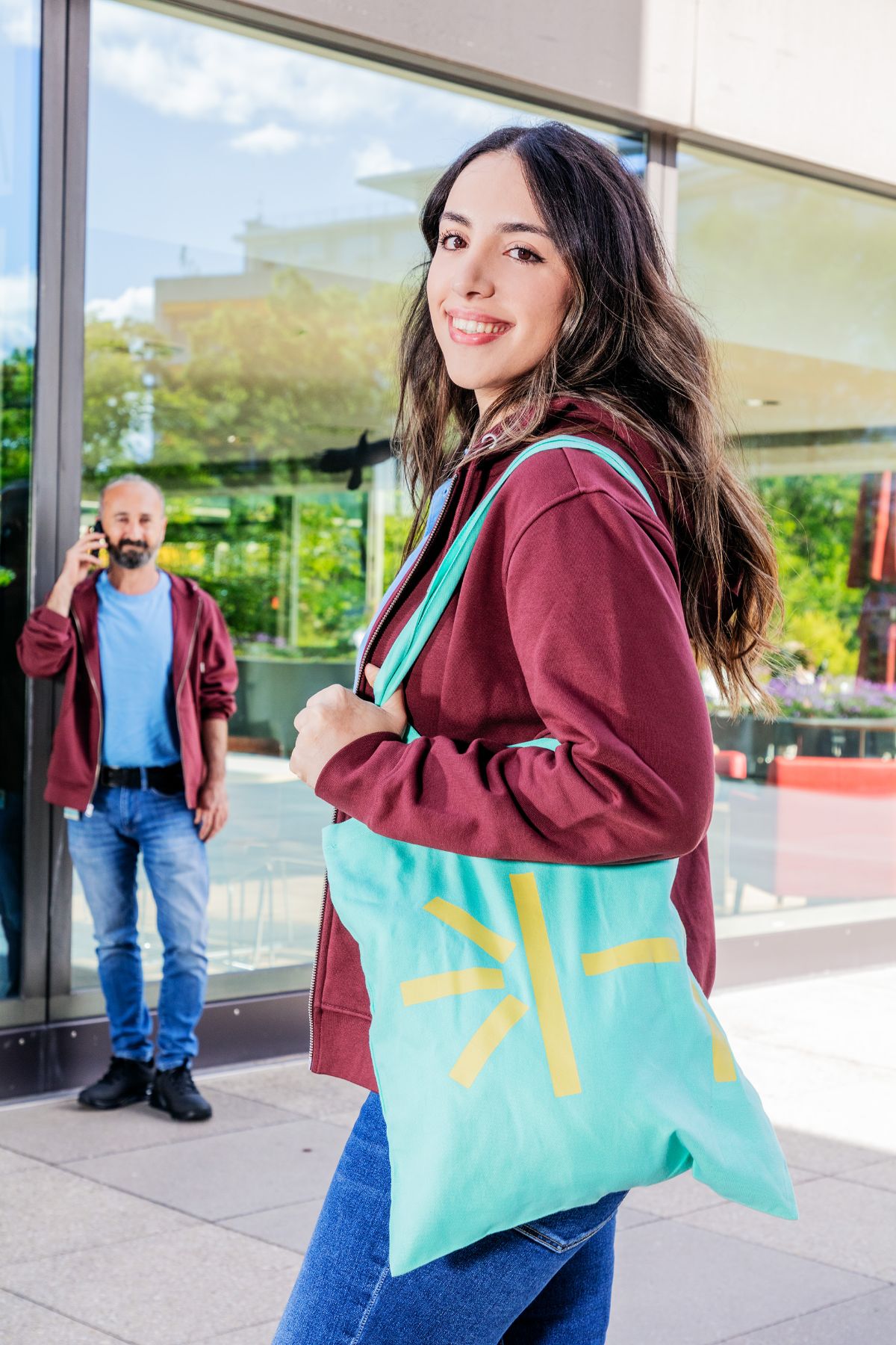 Mitarbeiterin mit weinrotem Hoodie und türkisfarbenem Totebag USB-Merchandise