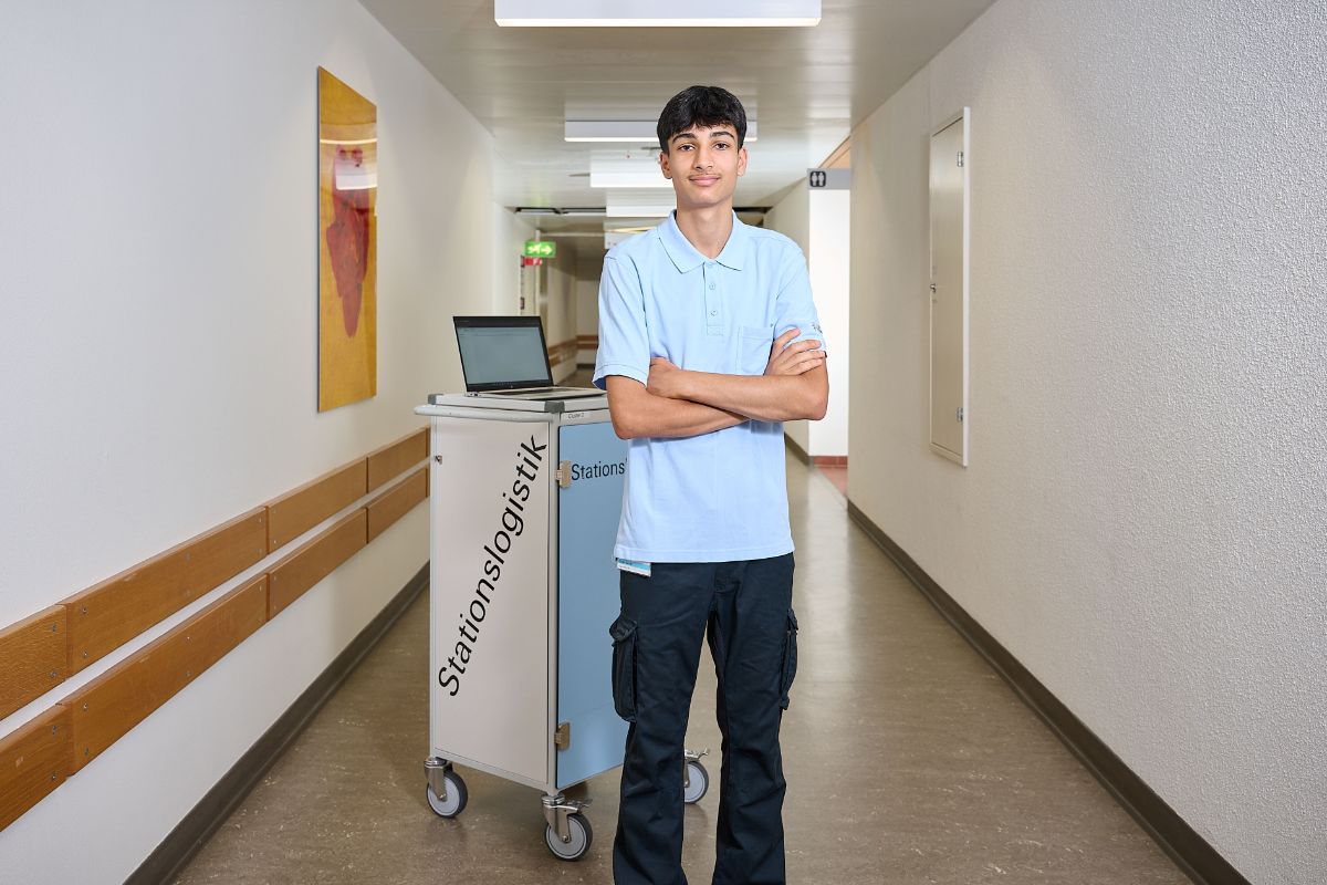 Logistikerin EFZ in Ausbildung steht mit verschränkten Händen vor einem Wagen der Stationslogistik