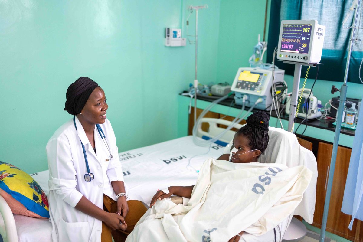 Pflegerin sitzt auf dem Patientenbett und betreut eine junge Patientin in Ifakara, Tansania